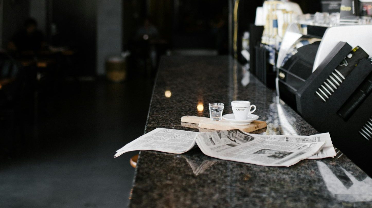 Newspaper on bar near empty coffee cup.